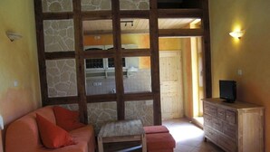 Un salon chaleureux avec un mur en pierre, un banc en bois, un canapé rouge et un meuble en bois abritant un téléviseur.