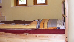 Un lit simple avec un cadre en bois, deux fenêtres au-dessus et un mur uni.