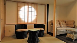 Een kamer met een tatami vloer, een salontafel met kussens, een bank met kussens en een groot raam met uitzicht.