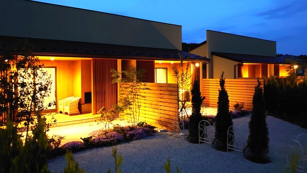 Een modern huis met een goed verlichte entree, een overdekte zithoek buiten en een grindpad.