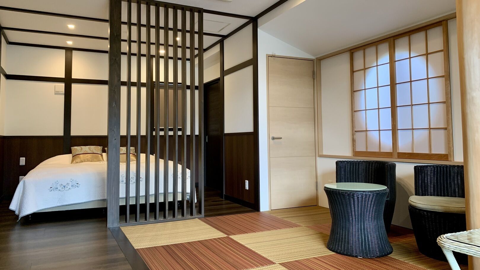 Habitación de hotel con cama, separador, puerta corredera japonesa tradicional, una mesita y dos sillas.