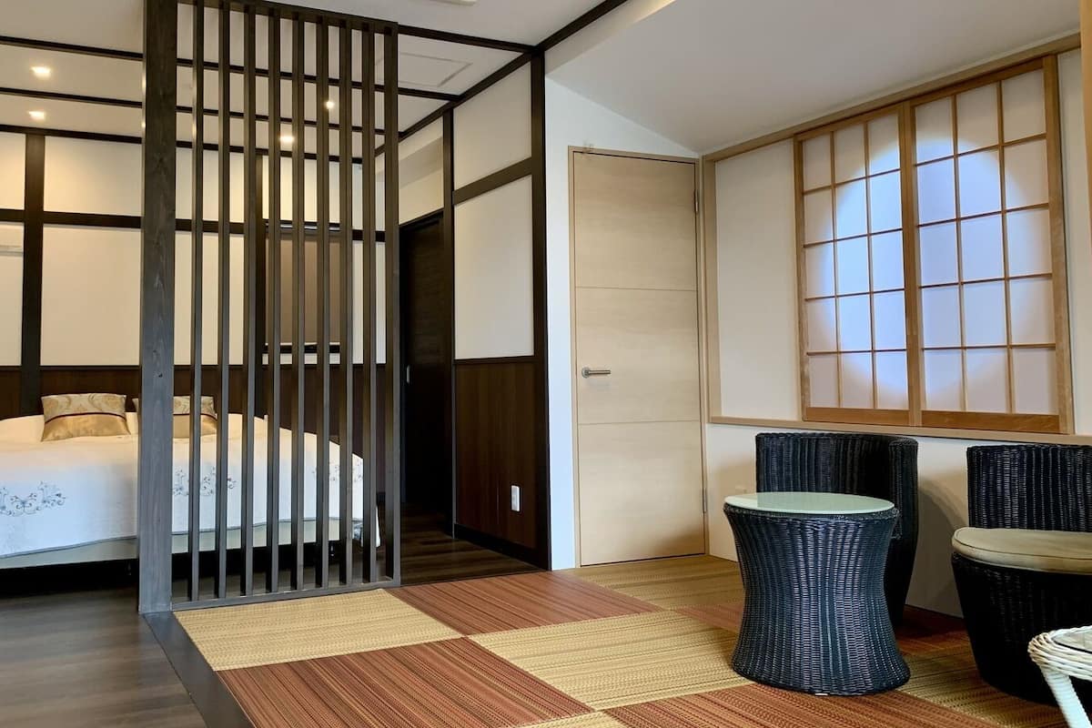 Ein Hotelzimmer mit Bett, einer Trennwand, einer traditionellen japanischen Schiebetür, einem kleinen Tisch und zwei Stühlen.