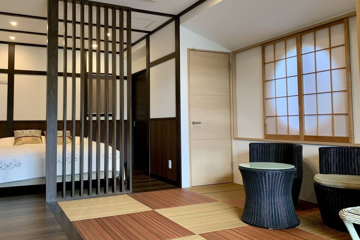 Habitación de hotel con cama, separador, puerta corredera japonesa tradicional, una mesita y dos sillas.
