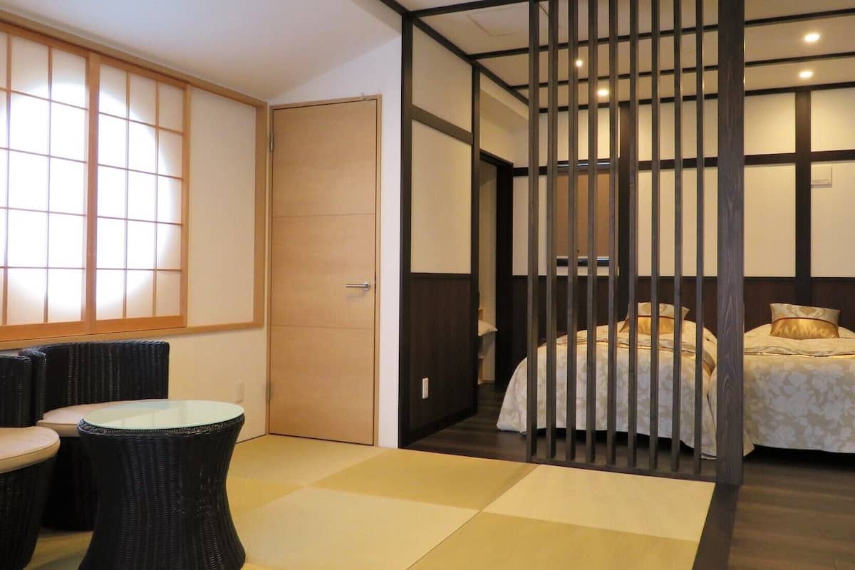 Ein traditionell japanisch eingerichteter Raum mit Tatami-Boden, einem niedrigen Bett mit floralem Überwurf und einer Schiebetür zu einem Badezimmer.