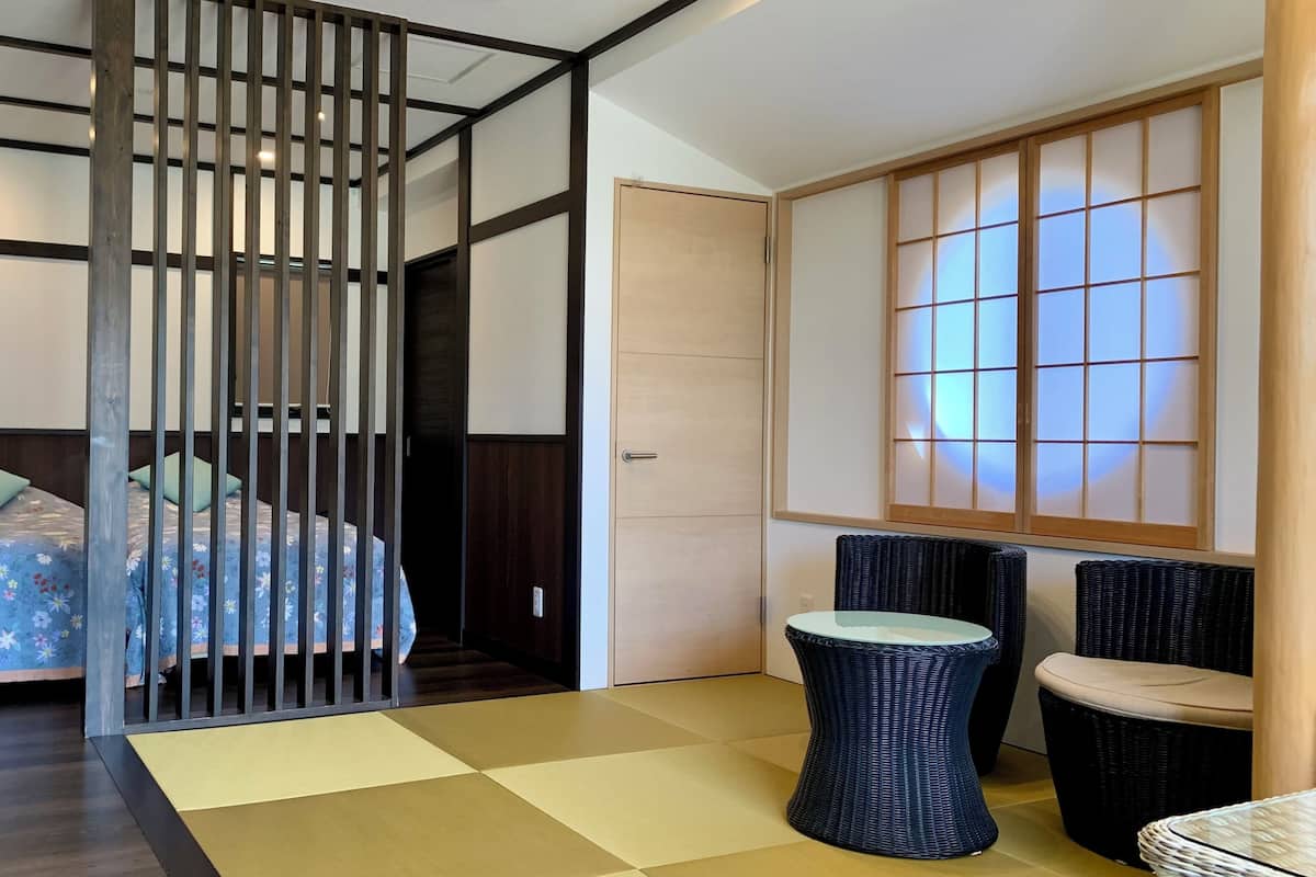Una habitación con cama, separador, suelo de tatami, puerta corredera y vistas a través de un shoji.