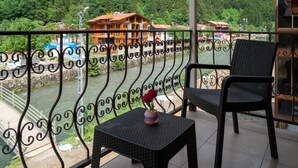 Un balcón con vista al río, dos sillas de mimbre y una mesita con un florero.