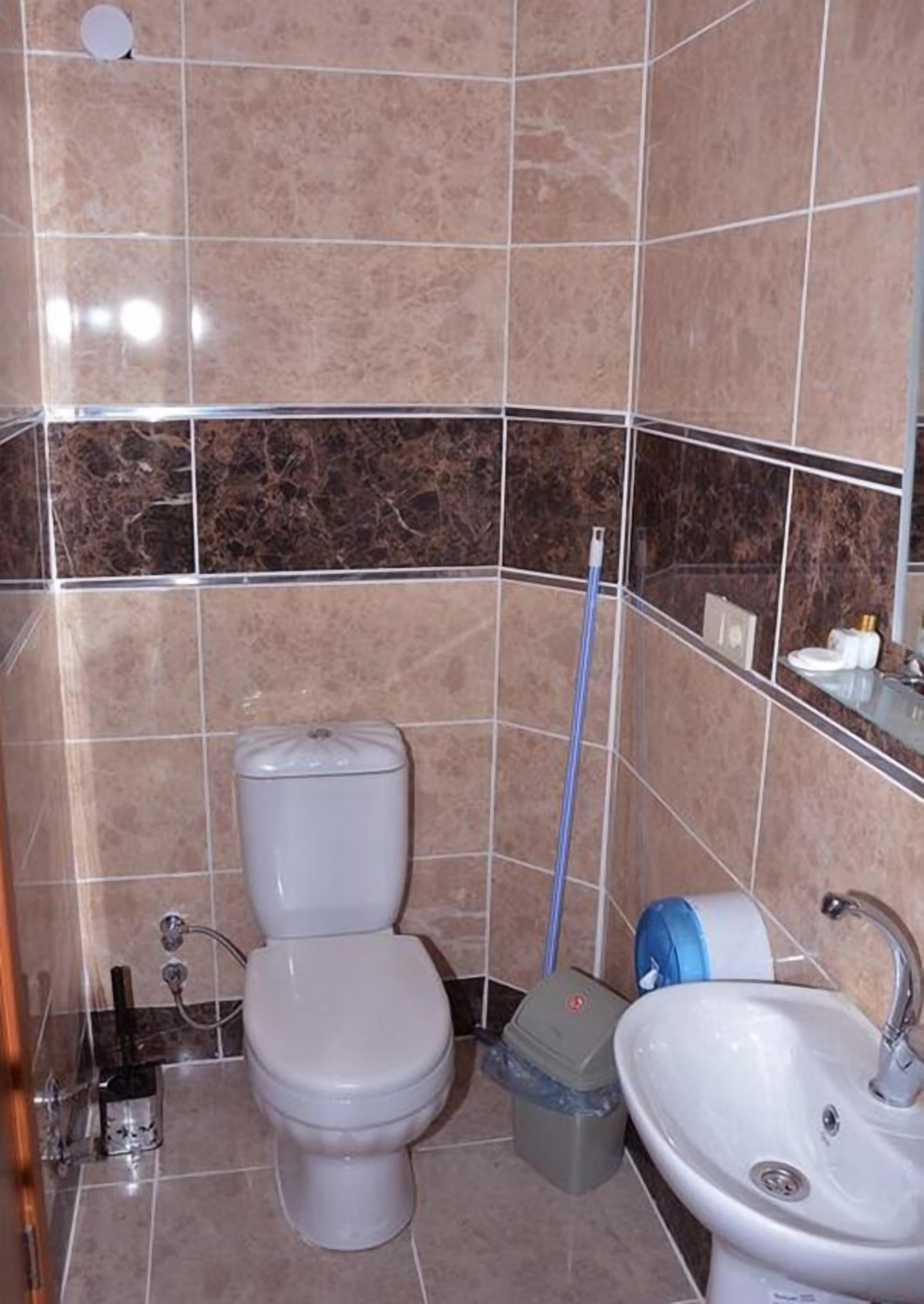 A bathroom with a toilet, sink, and a mop leaning against the wall.