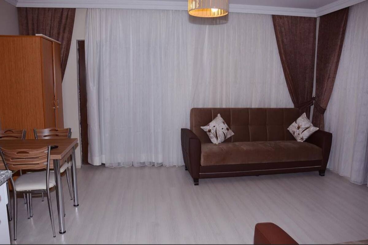 Un salon avec un canapé marron, des rideaux blancs et une table à manger en bois, accompagnée de chaises.