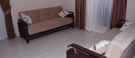 Una sala de estar con un sofá, una silla y un ventanal con cortinas.