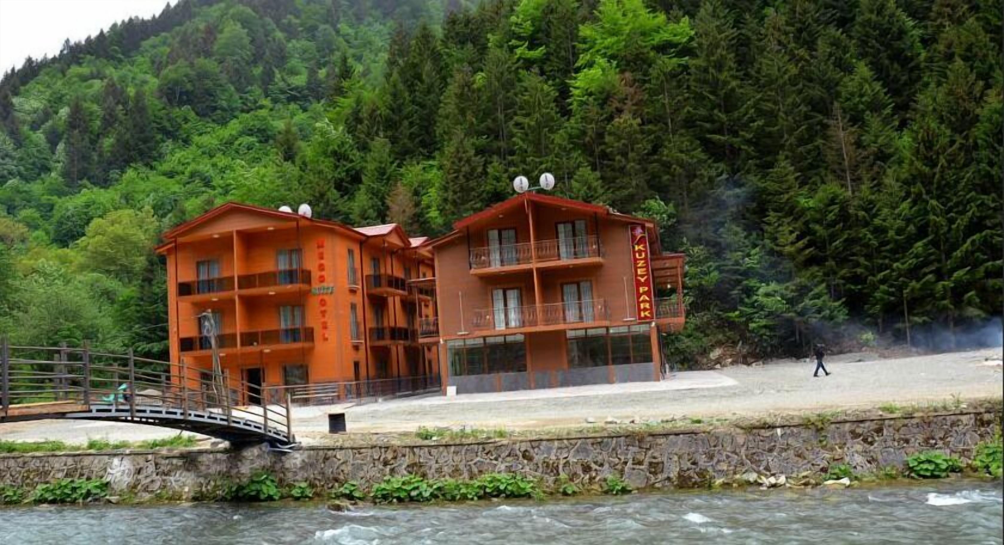 A hotel with a stone facade, multiple balconies, and a view of a forested hillside.