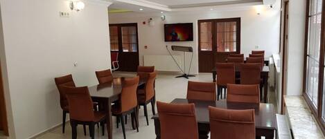 A conference room with multiple tables and chairs, large windows, and a television screen.