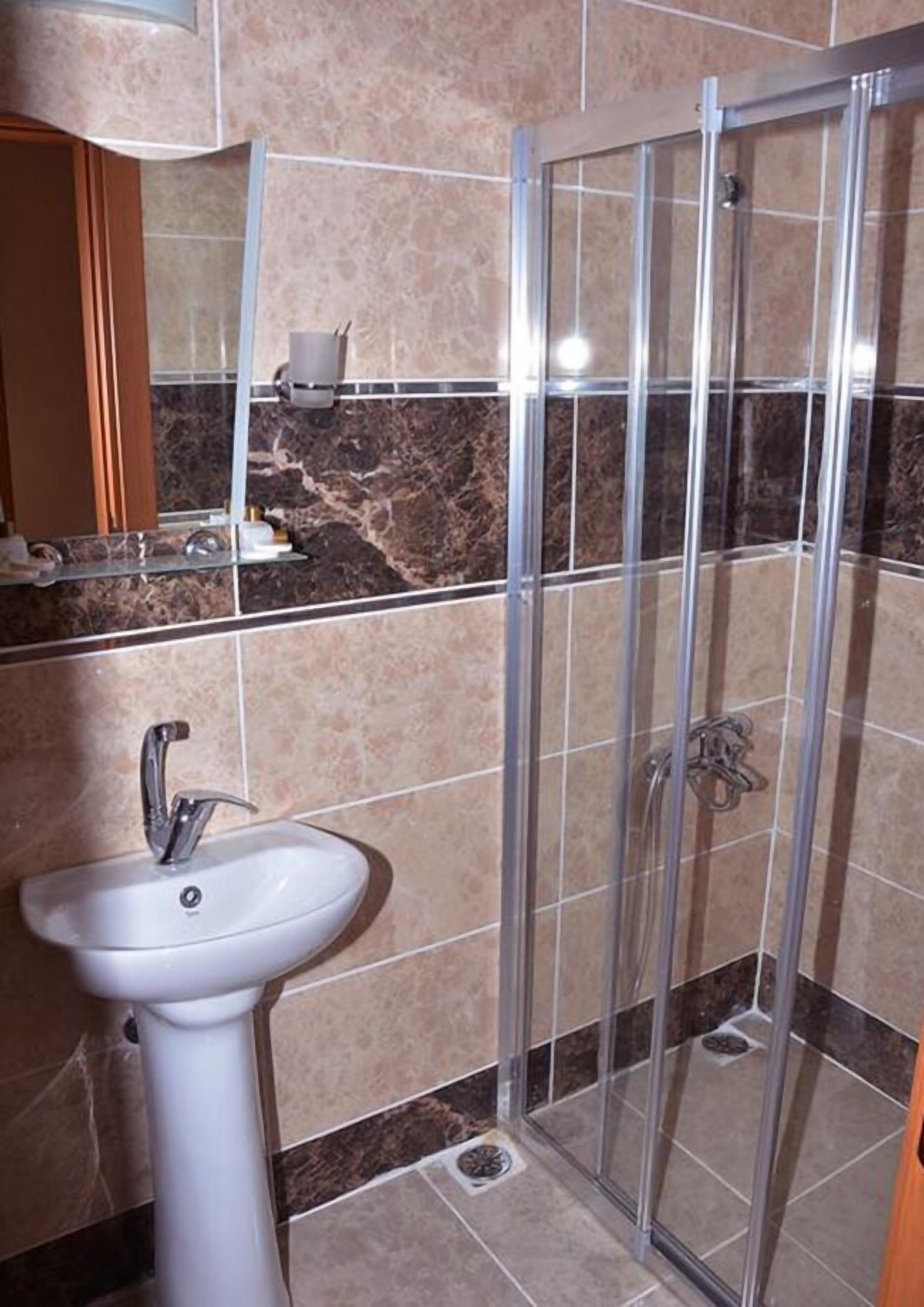 Ein Badezimmer mit einem weißen Waschbecken, einer Duschkabine aus Glas und einer Wand mit Marmorfliesen.