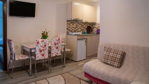 Un espacio habitable compacto con un sofá, una mesa de comedor con sillas de flores, una zona de cocina con microondas y un televisor de pantalla plana montado en la pared.