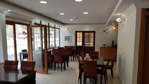 Un comedor amplio con varias mesas y sillas, una puerta de cristal que da al exterior y una pequeña cocina americana en la esquina.
