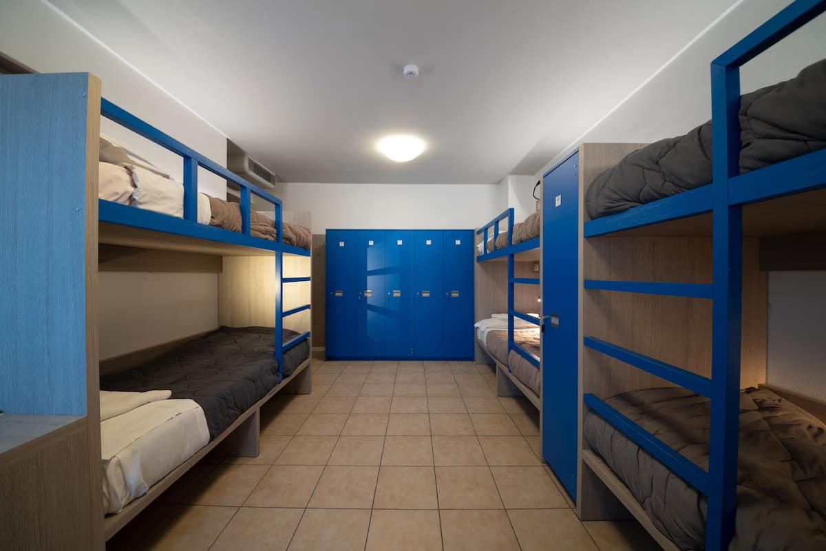 Ein Schlafsaalzimmer mit Etagenbetten, einem blauen Kleiderschrank und einem gefliesten Boden.