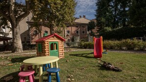 Une aire de jeux avec une cabane en bois, un toboggan et des tabourets colorés.