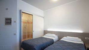 Une chambre avec deux lits, un espace douche et un interrupteur sur le mur.