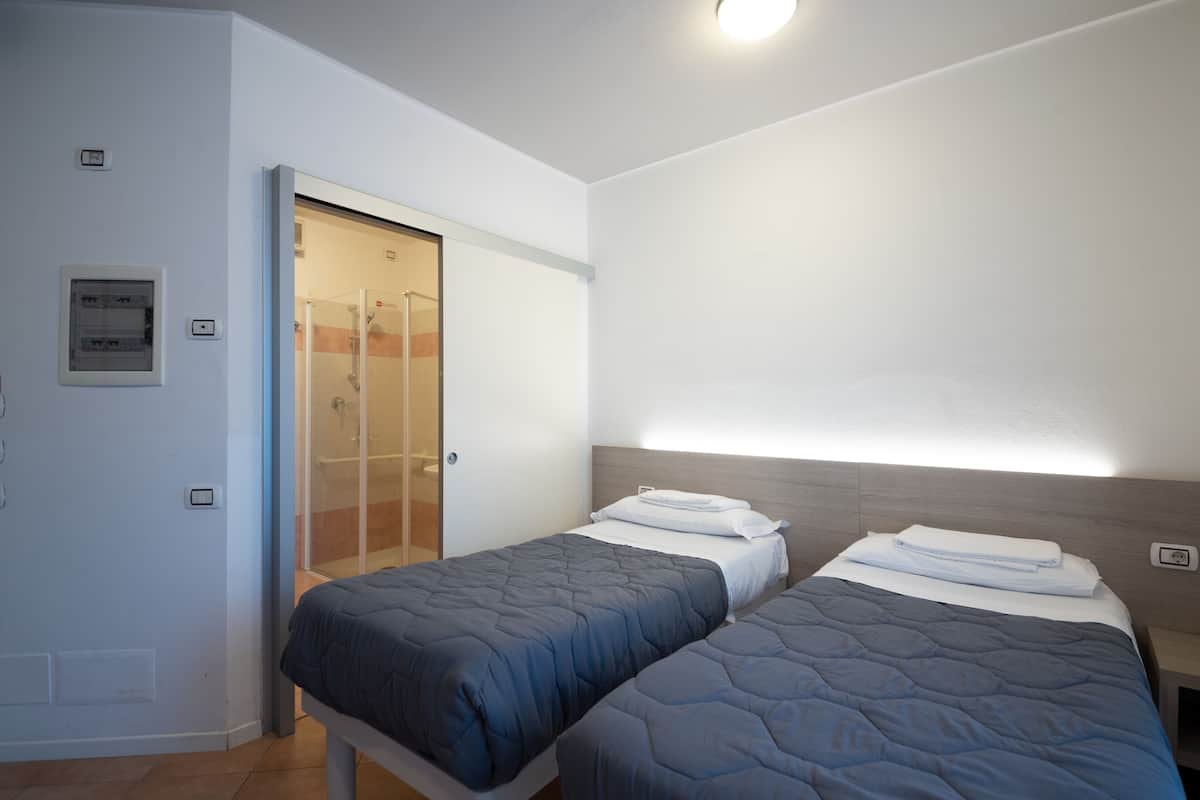 Ein Schlafzimmer mit zwei Betten, einer Duschkabine und einem Lichtschalter an der Wand.