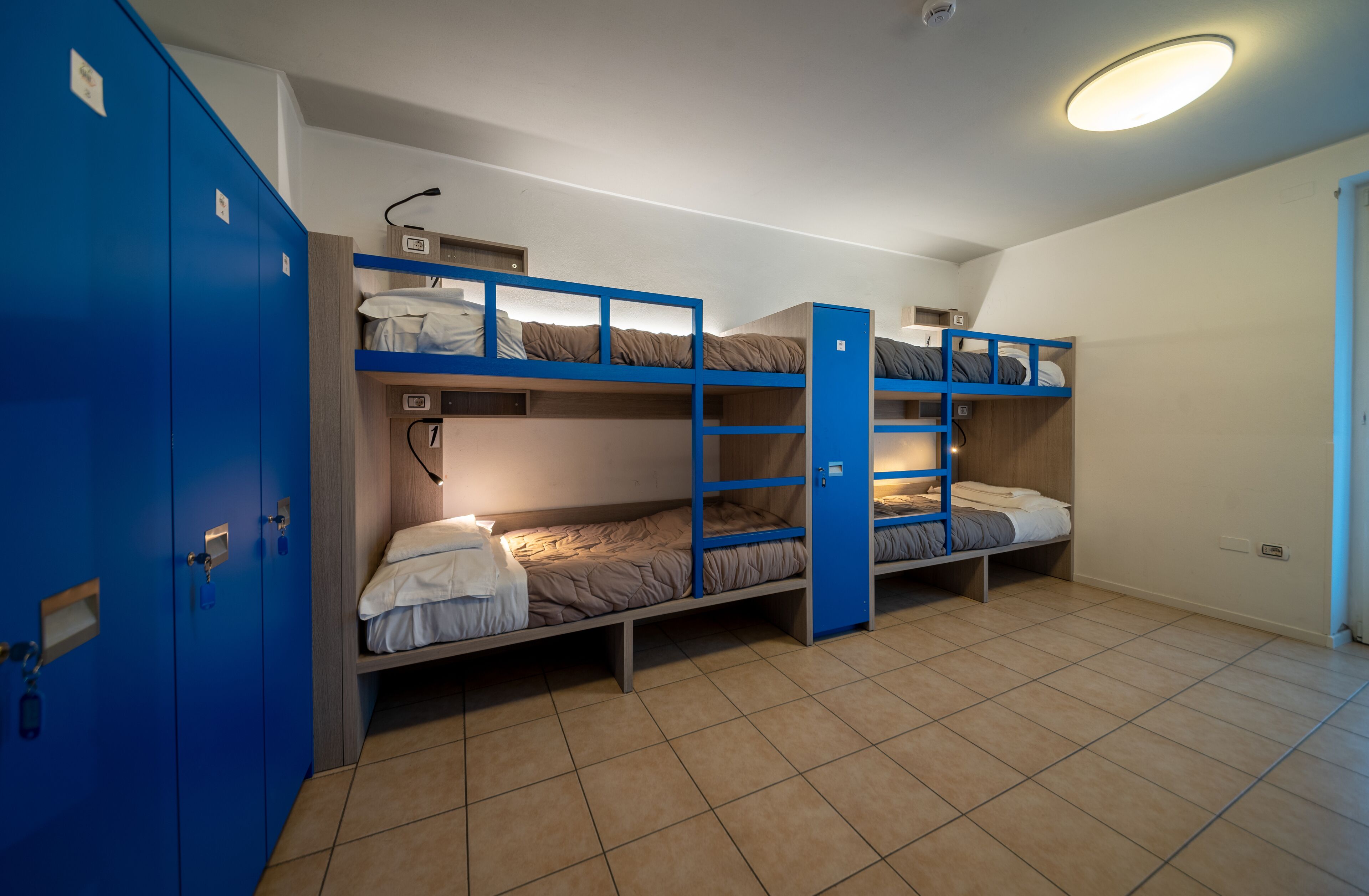 A dormitory room with bunk beds, a blue wardrobe, and a ceiling light.