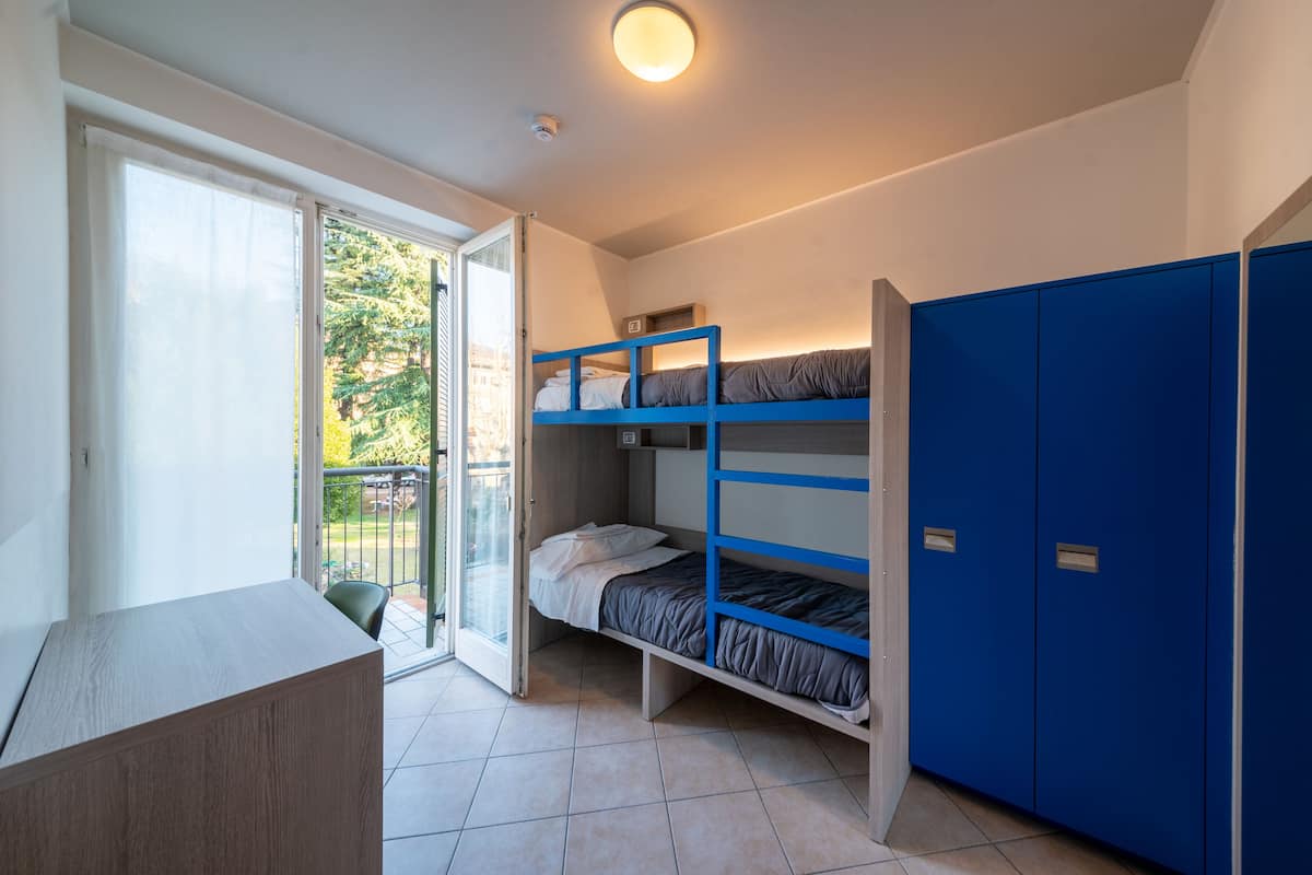 Ein Schlafsaalzimmer mit Etagenbetten, einem Schreibtisch und einer Glastür zu einem Balkon.