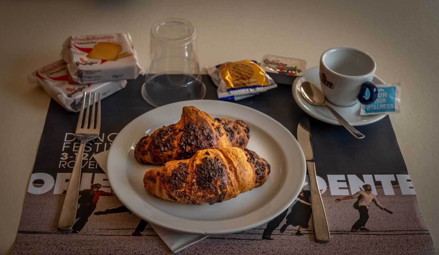 Une table mise pour le petit-déjeuner avec des croissants, une tasse de café et une nappe décorative ornée d’une affiche.