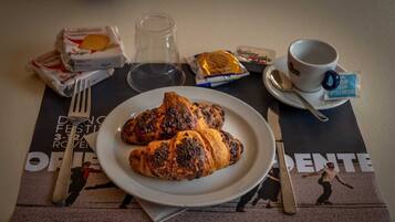 Une table mise pour le petit-déjeuner avec des croissants, une tasse de café et une nappe décorative ornée d’une affiche.