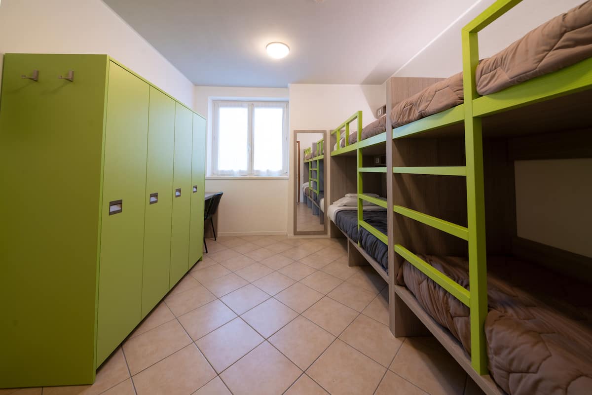 Ein Schlafsaalzimmer mit Etagenbetten, einem grünen Kleiderschrank und einem Fenster.