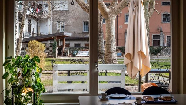 Un coin repas avec une table dressée pour deux personnes, une plante en pot et une vue sur la rue.