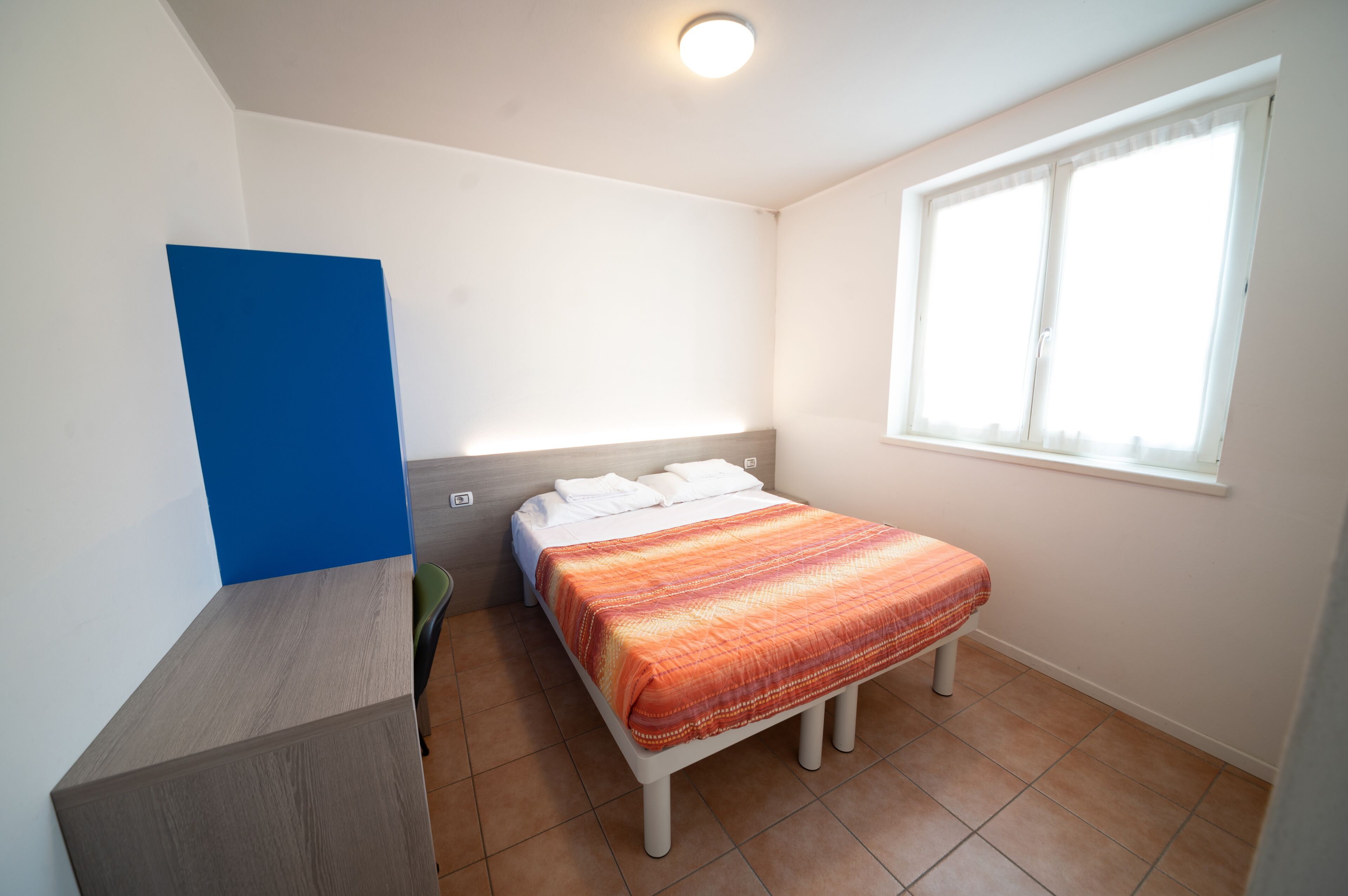 Ein kleines, sauberes Zimmer mit einem Bett, einem Schreibtisch und einem Fenster.