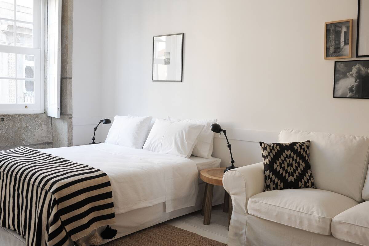A minimalist bedroom with a bed, a bedside table, a lamp, and a couch.