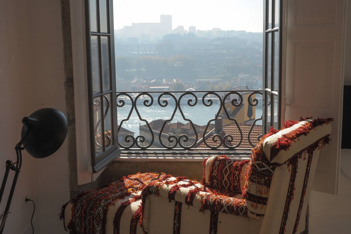 A room with a view of a cityscape through a window with a decorative iron railing.