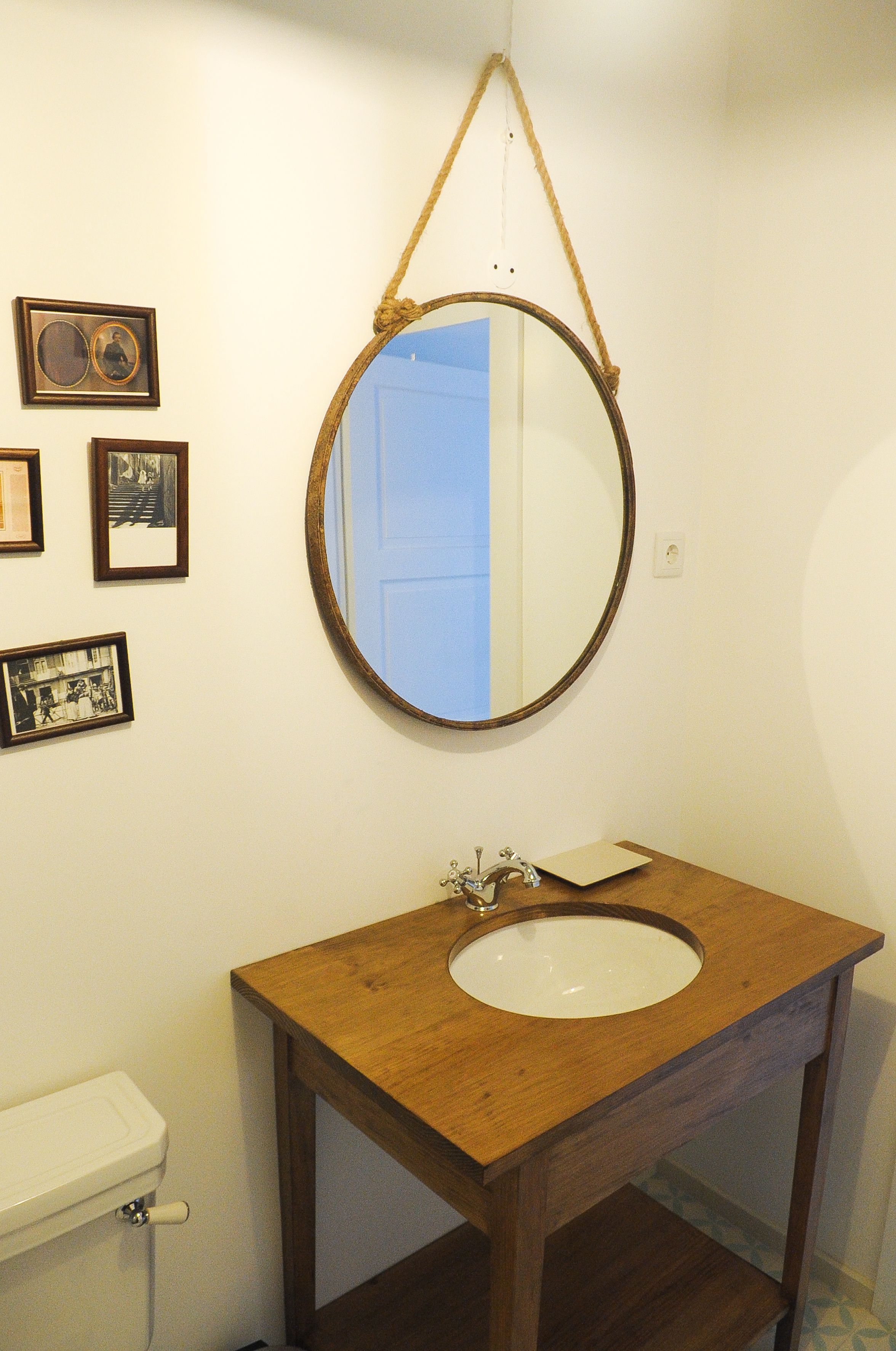 Un baño con tocador de madera, un espejo redondo y cuadros enmarcados en la pared.