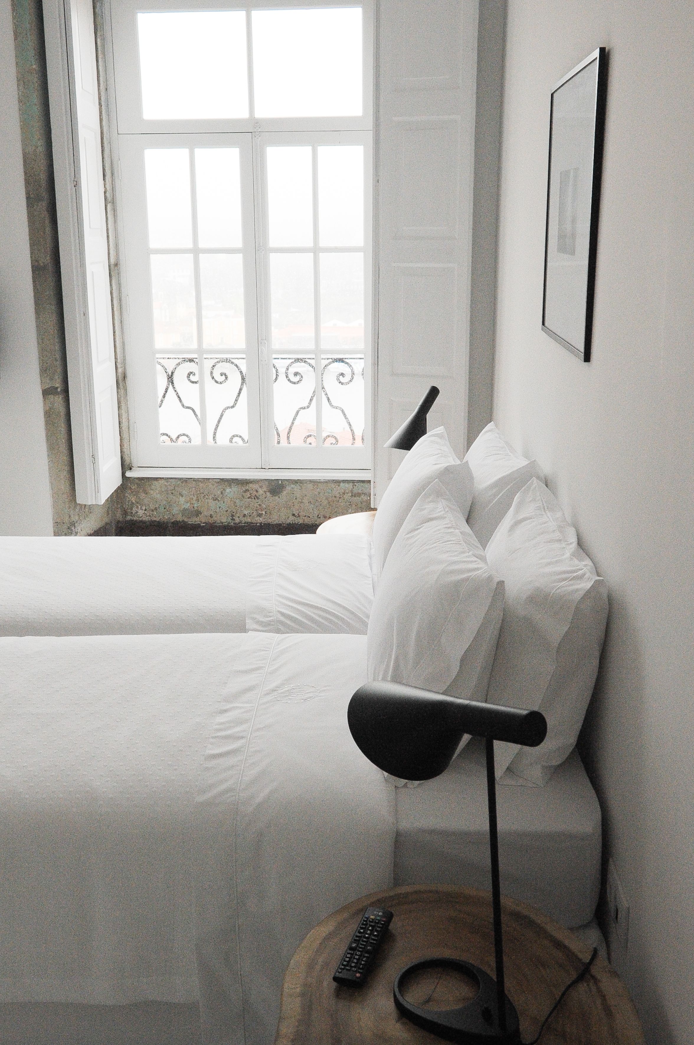 Ein Schlafzimmer mit einem Bett, einem Nachttisch mit Lampe, einer Fernbedienung und einem Fenster mit Blick auf einen Balkon.