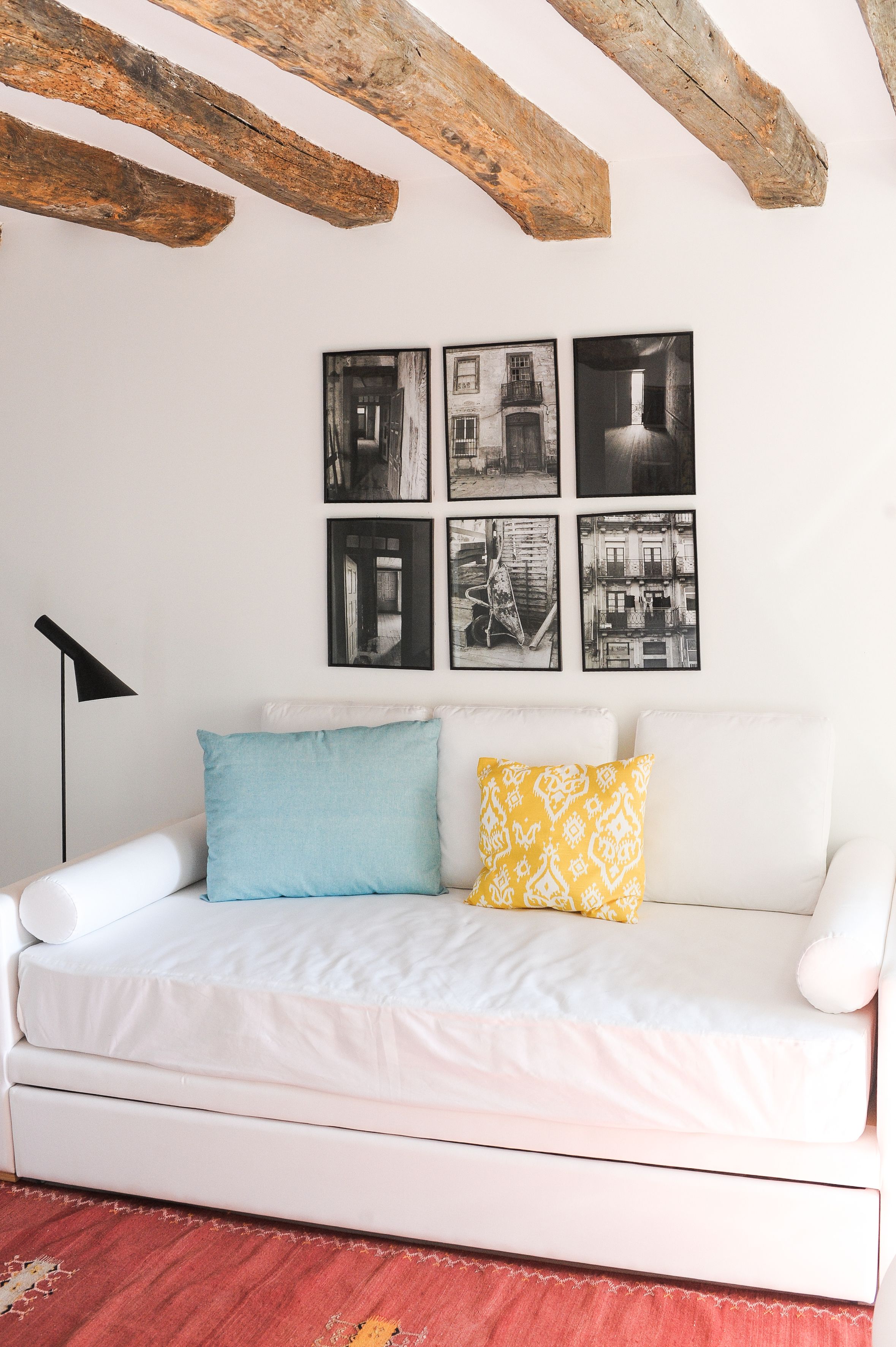 Un canapé blanc avec deux coussins, un lampadaire noir et six photographies en noir et blanc accrochées au mur.