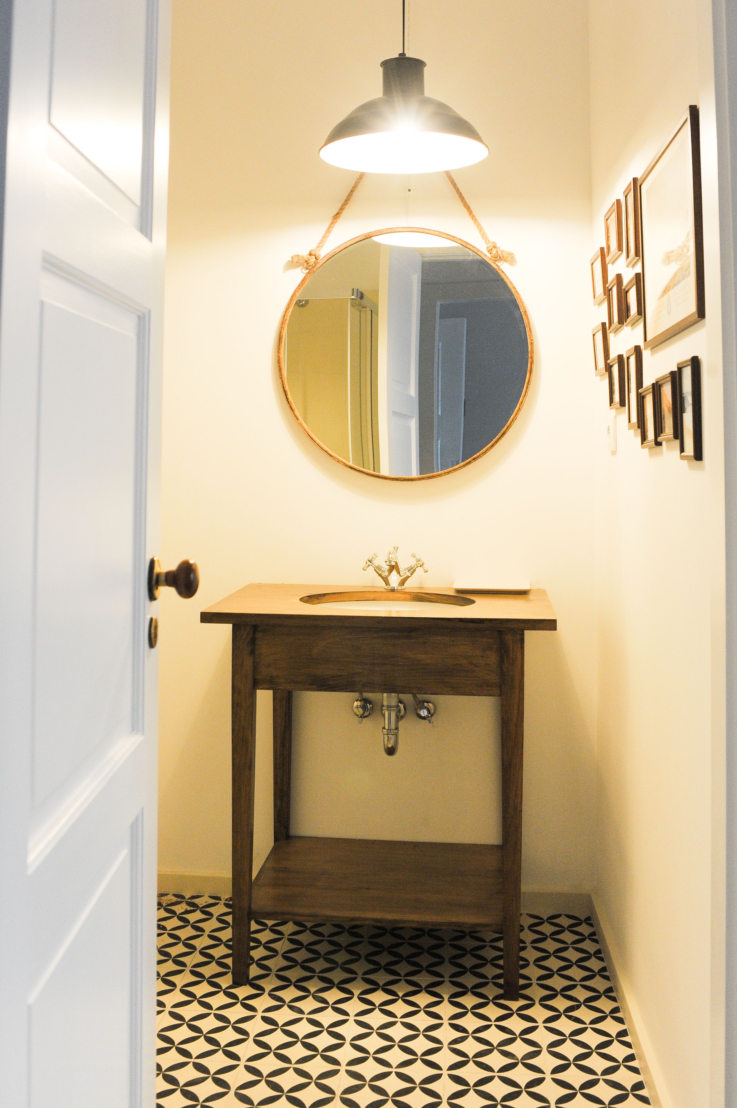 A bathroom with a round mirror, wooden vanity, and patterned floor tiles.