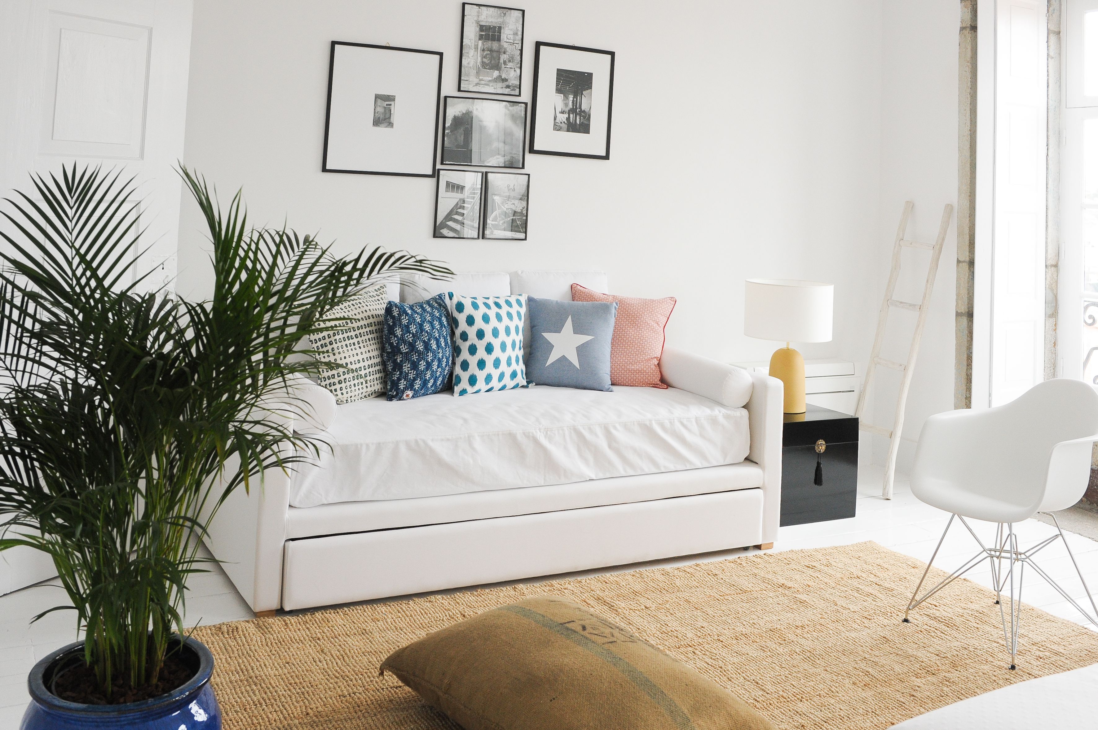 A modern living room with a white sofa, patterned cushions, a potted plant, and framed pictures on the wall.