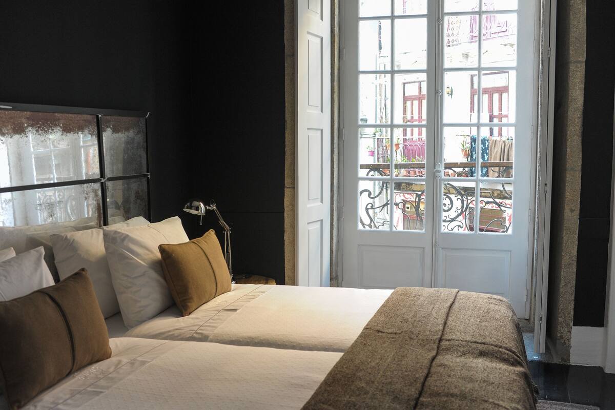 A bedroom with two beds, a large window, and a view of the street outside.