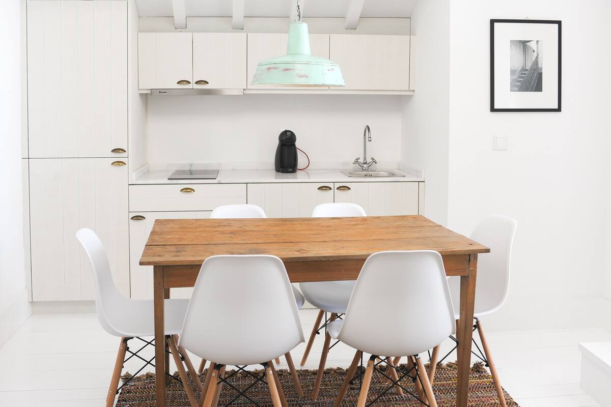 A modern kitchen with white cabinets, a wooden table, and white chairs.