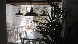 A rustic dining area with wooden tables and white chairs, large hanging pendant lights, and a potted plant. - Mo House (Porto)