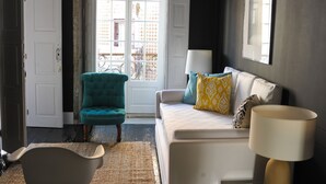 A room with a teal armchair, a white sofa with patterned cushions, a lamp, and a view of a balcony with a bicycle. - Mo House (Porto)