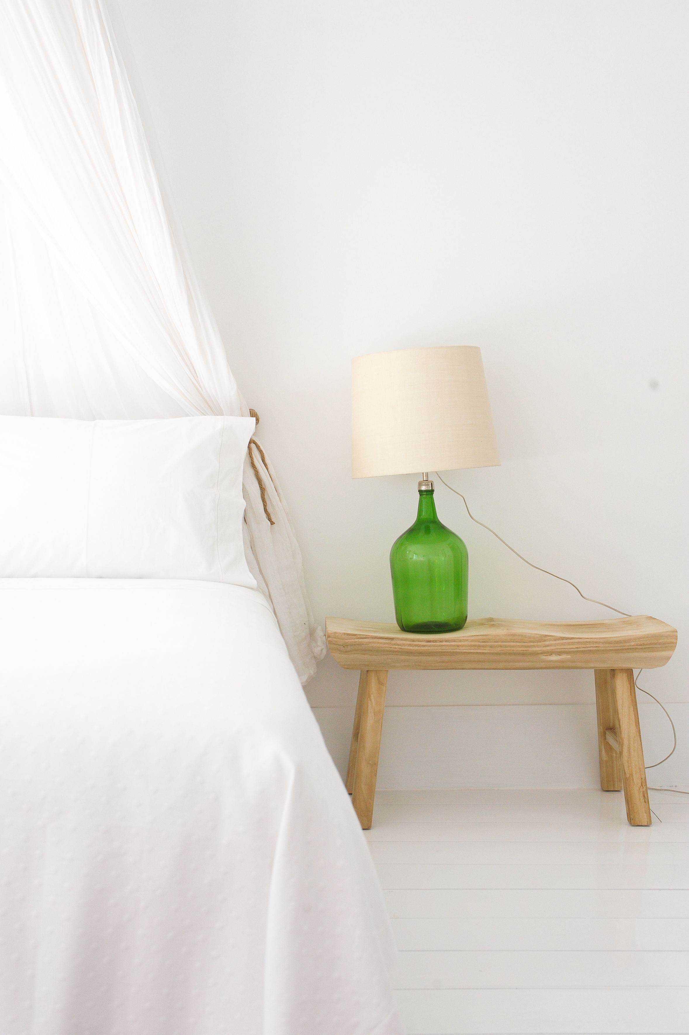 A bed with white bedding, a green lamp on a wooden nightstand, and a white wall.