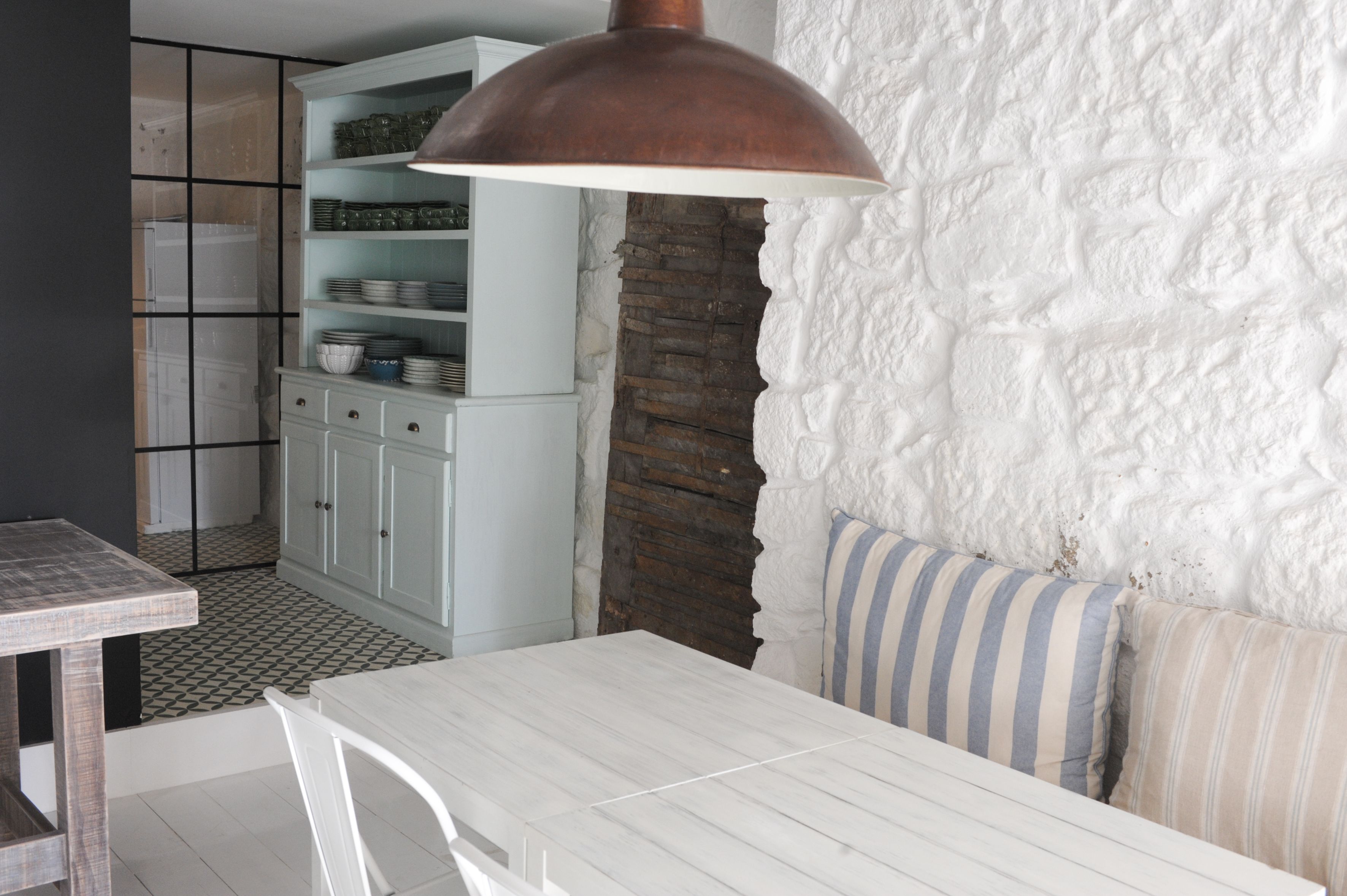 A kitchen with white cabinets, a stone wall, and a hanging copper light fixture.