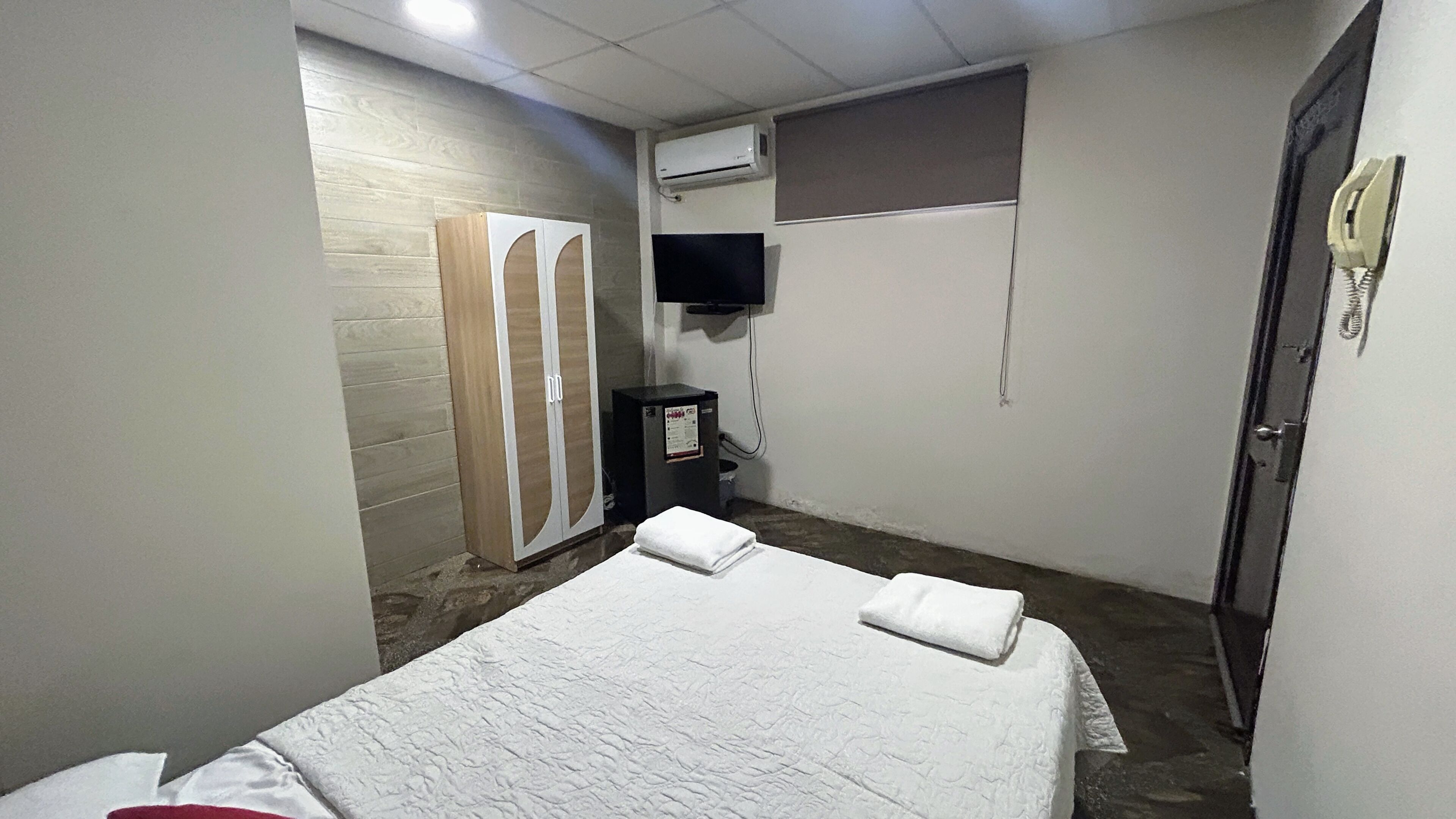 Un dormitorio con cama, armario, televisor, aire acondicionado y teléfono.