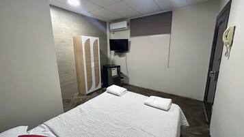 Un dormitorio con cama, armario, televisor, aire acondicionado y teléfono.