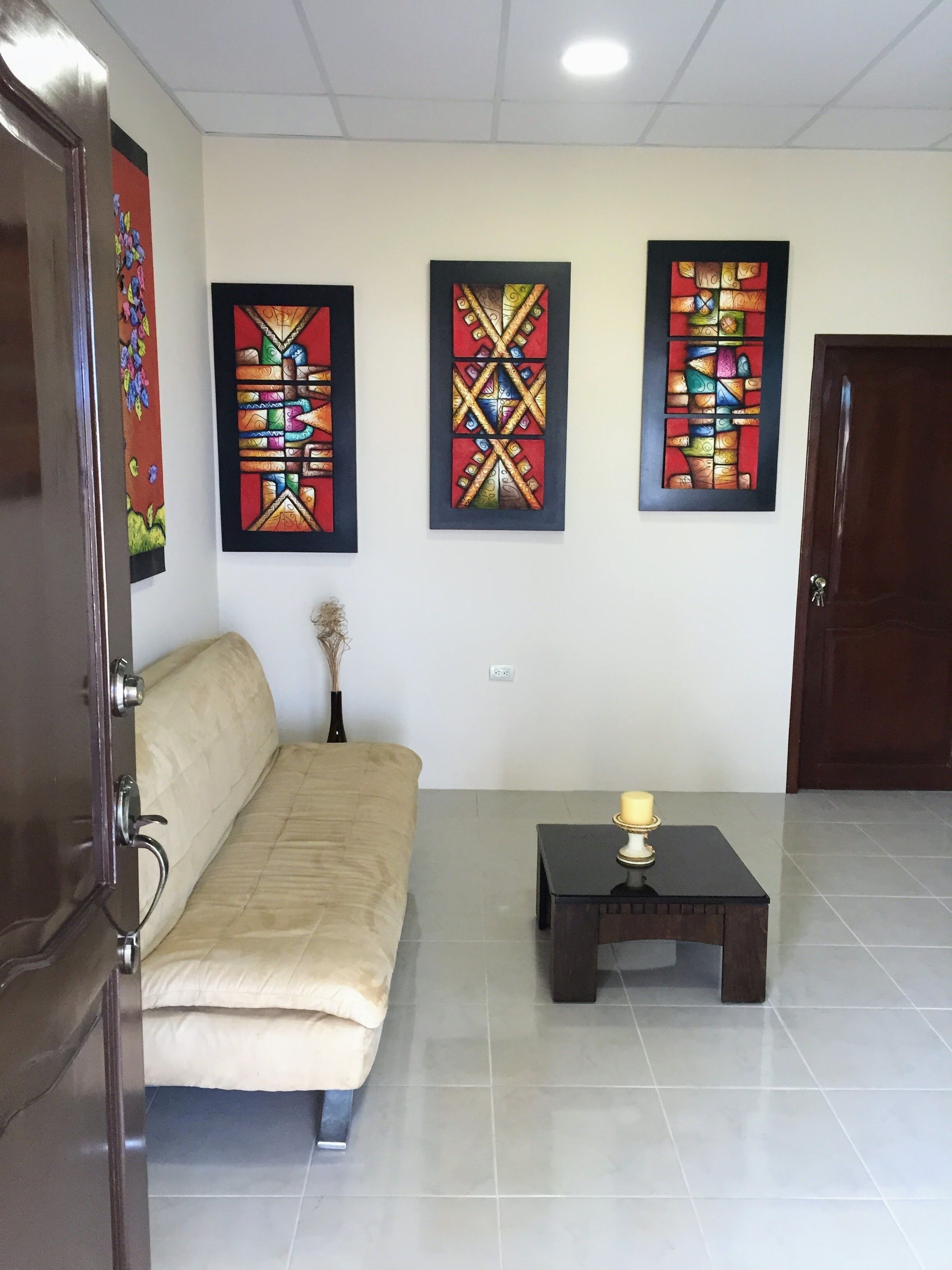Una habitación con un sofá color beige, una mesita con una vela y tres cuadros abstractos en la pared.