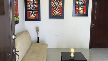 Una habitación con un sofá color beige, una mesita con una vela y tres cuadros abstractos en la pared.