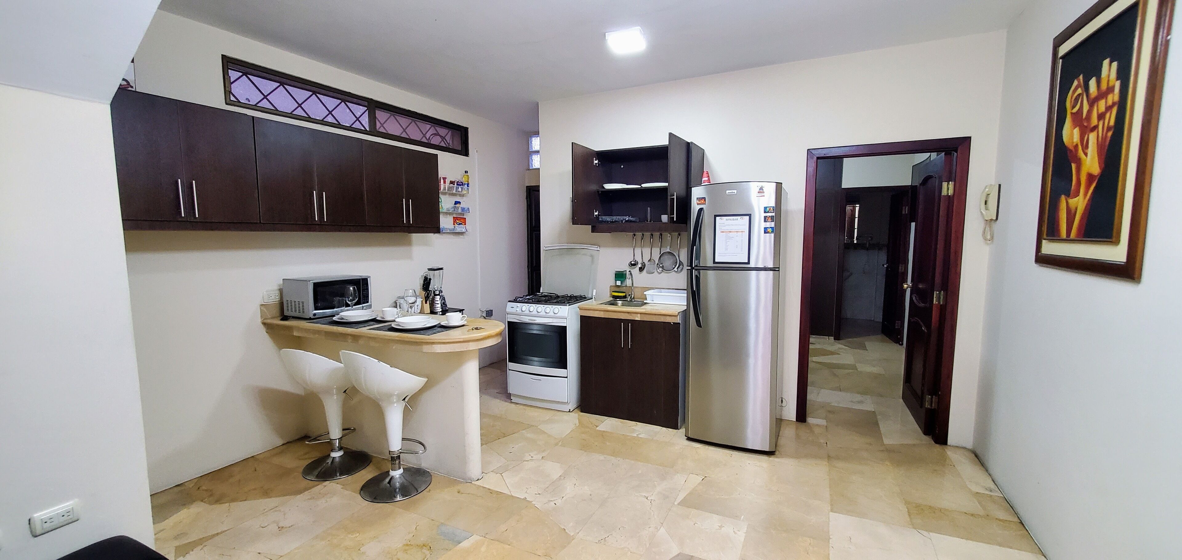 Cocina compacta equipada con refrigerador, estufa, microondas y dos taburetes de bar.