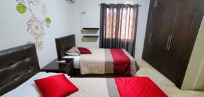 A bedroom with two beds, a wardrobe, a nightstand, and a wall decoration. - NCG Suite 1 (Guayaquil)