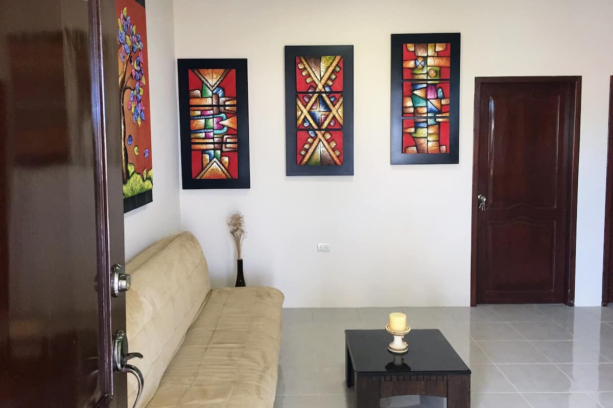 A room with a beige sofa, a small table with a candle, and three framed artworks on the wall.