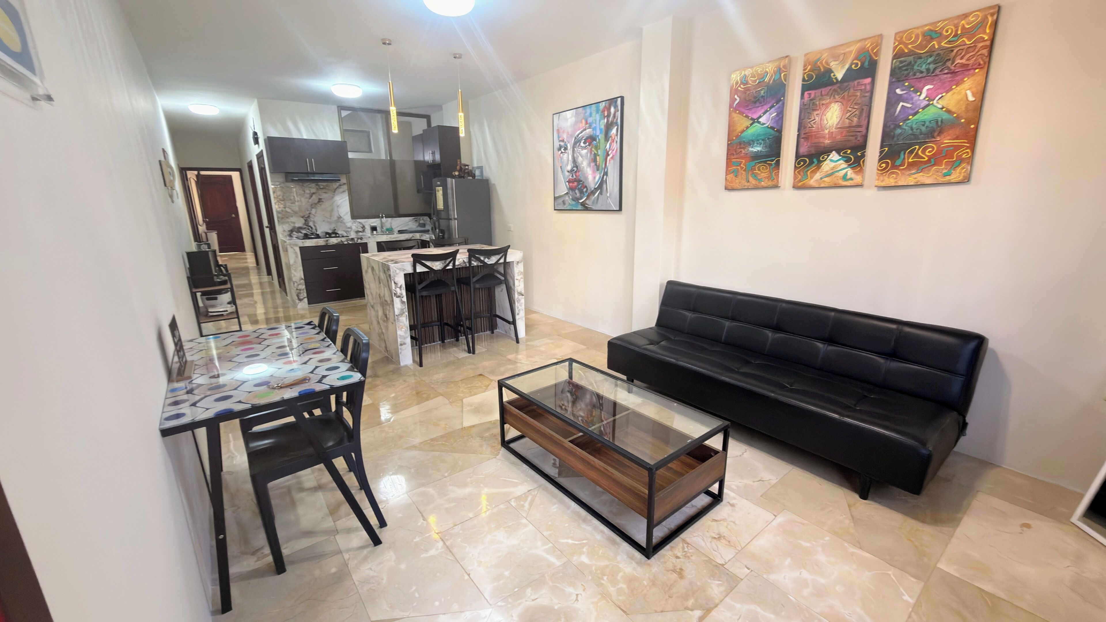 A modern living room with a black sofa, a glass coffee table, and a dining area with a patterned table.